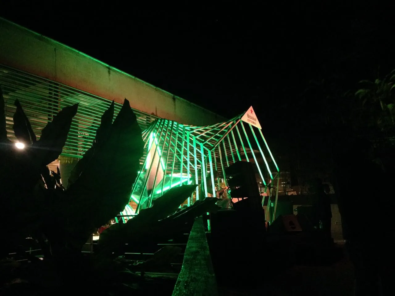 Externe Nachtansicht der Heineken-Bar-Installation mit der beleuchteten parametrischen Bambusstruktur, die sich vom Gebäude erstreckt.