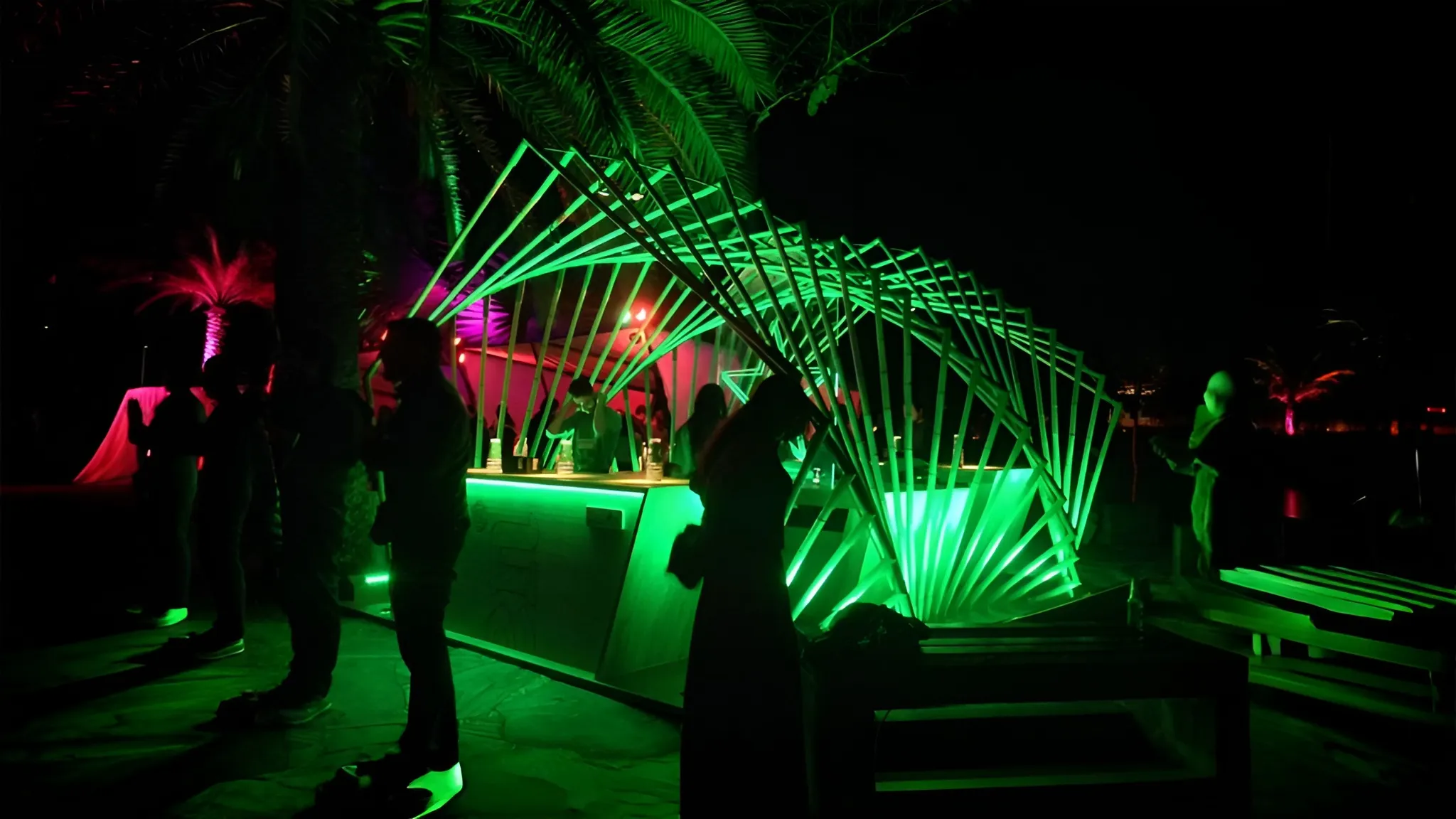 Nachtansicht der Heineken-Bar mit Besuchern, parametrische Bambusstruktur grün leuchtend mit umgebender tropischer Vegetation.
