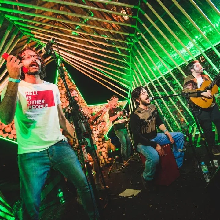 Band spielt auf der Heineken-Bühne, Musiker singen und spielen Gitarre unter der parametrischen Bambusstruktur, die in Grün beleuchtet ist.