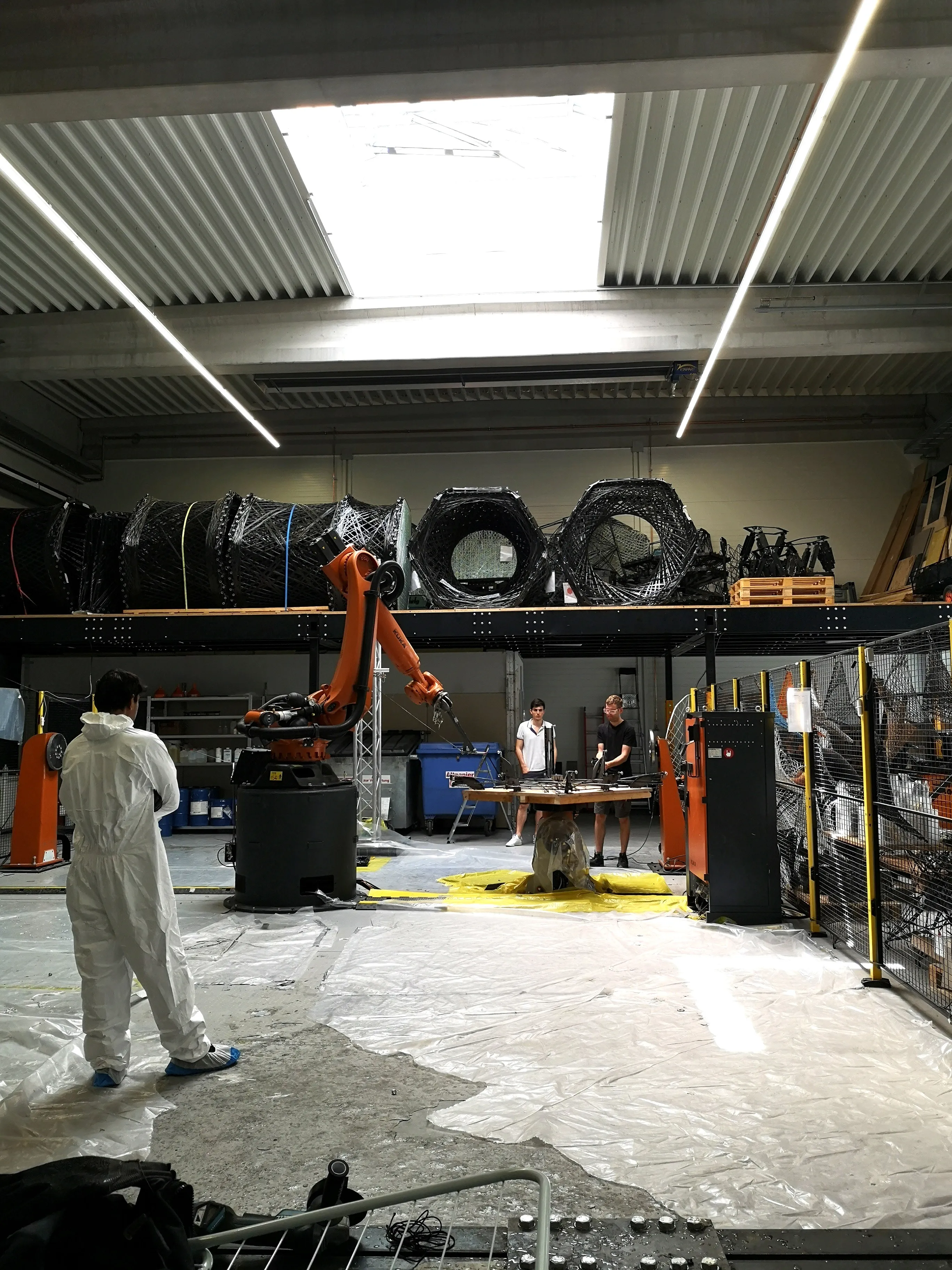 Daniel Nunes Locatelli in protective suit standing next to the KUKA robotic arm at ICD Stuttgart.