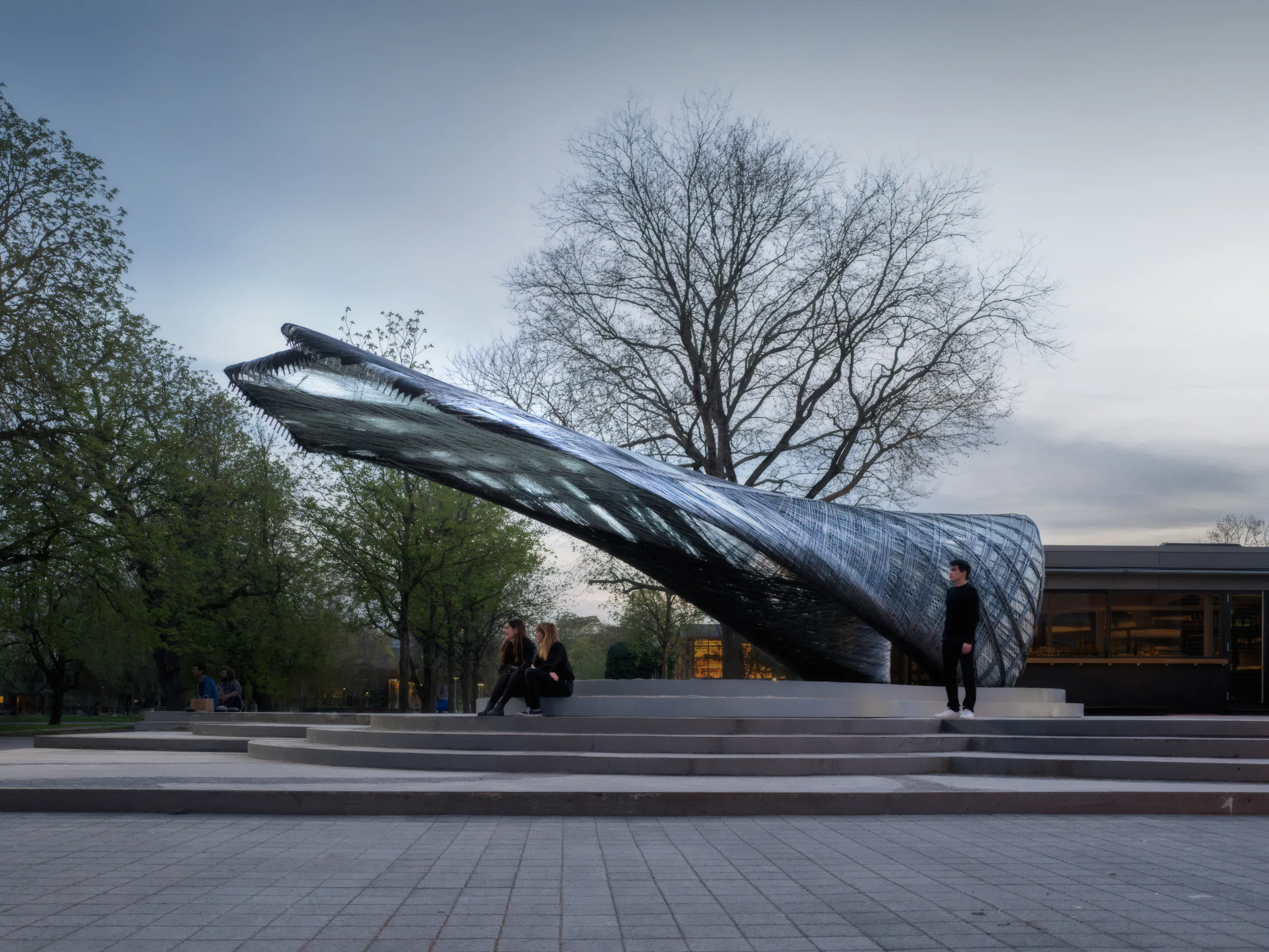 ICD/ITKE Research Pavilion 2016-17, auskragende Kohlefaserstruktur in der Abenddämmerung, mit Menschen ringsum