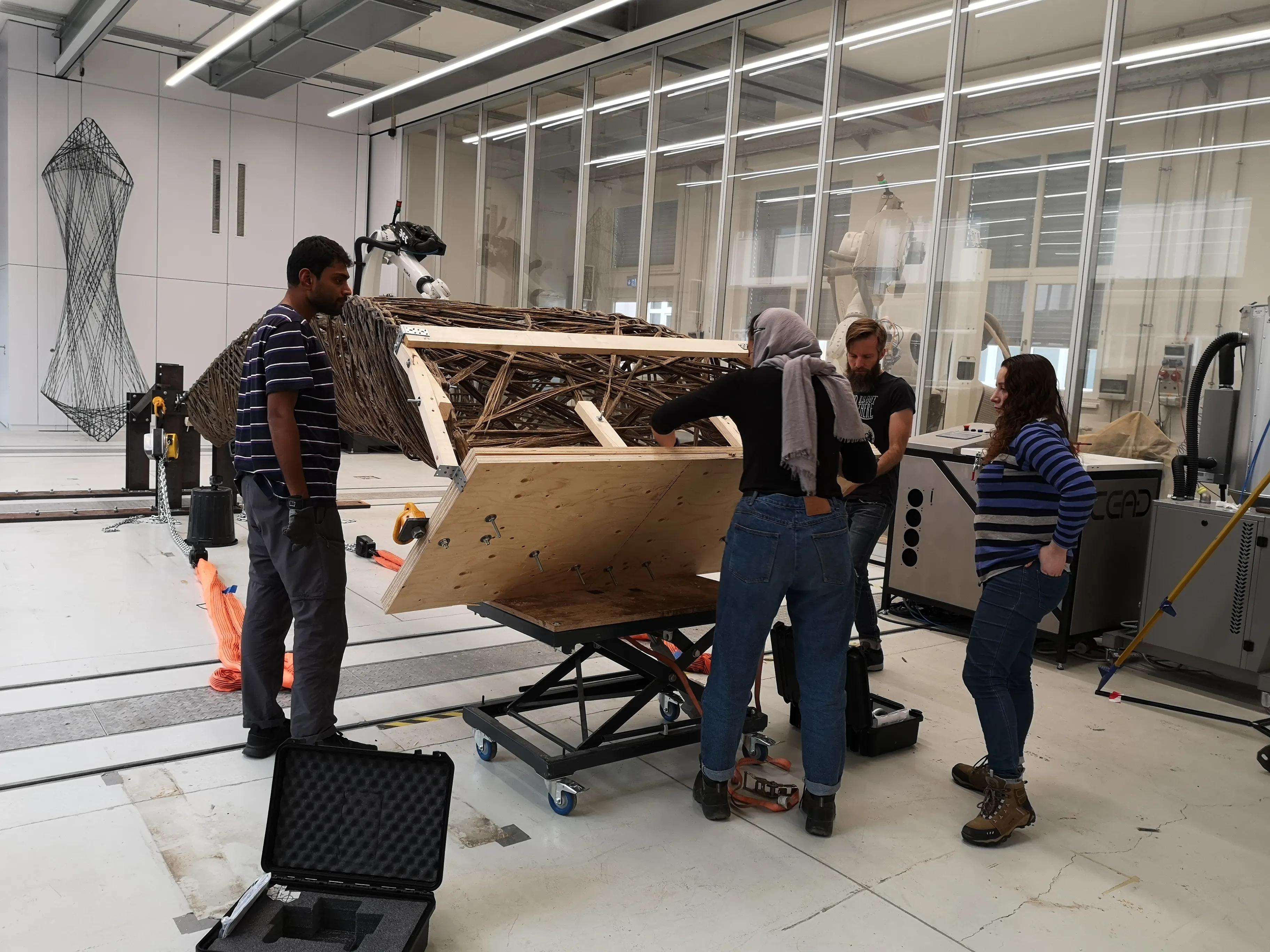 Research team preparing a natural fiber wound specimen for load testing at the ITKE lab. A carbon fiber tower prototype is visible in the background.