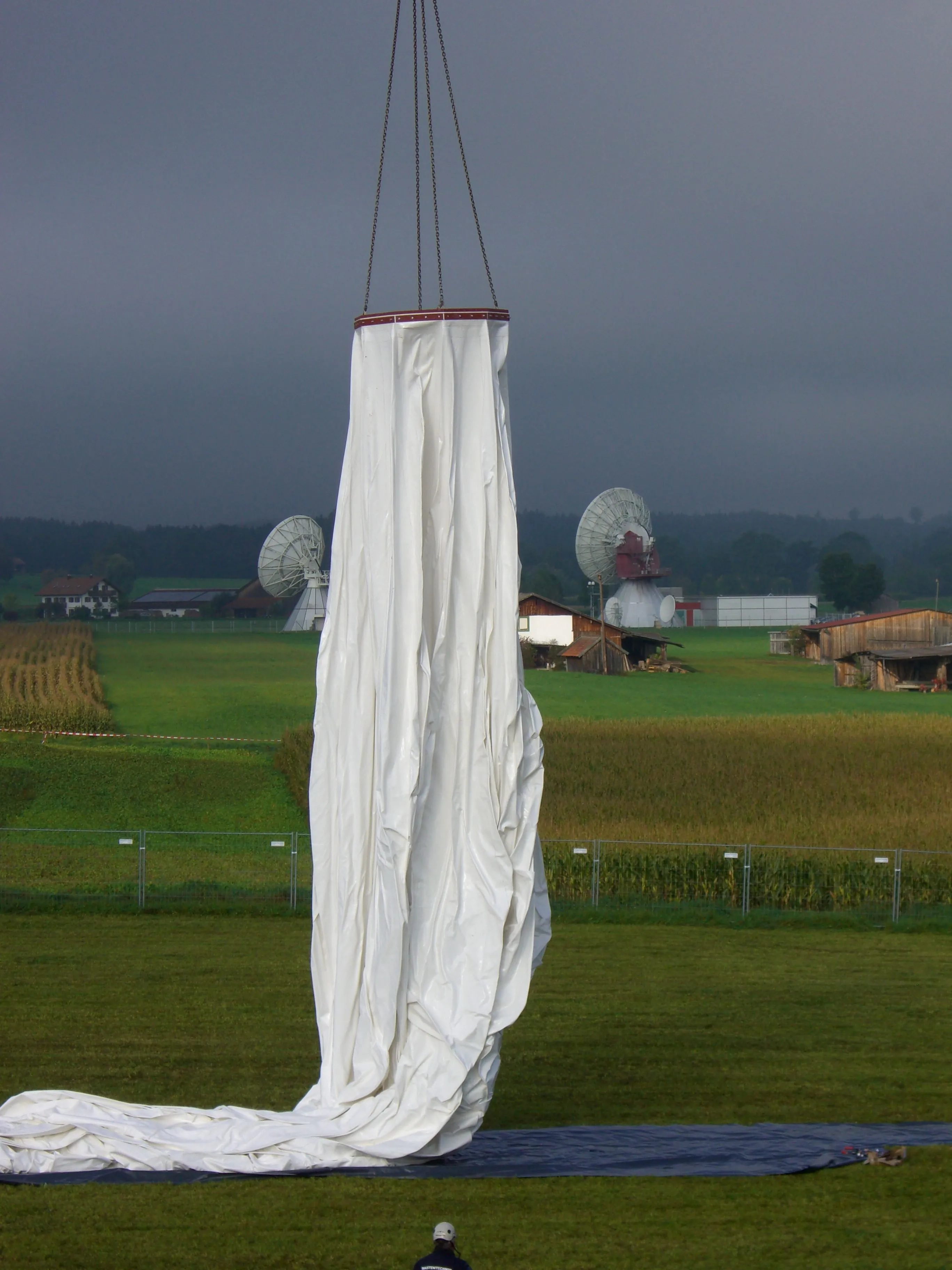 O fardo da membrana sendo levantado pelo guindaste, com antenas parabólicas ao fundo.