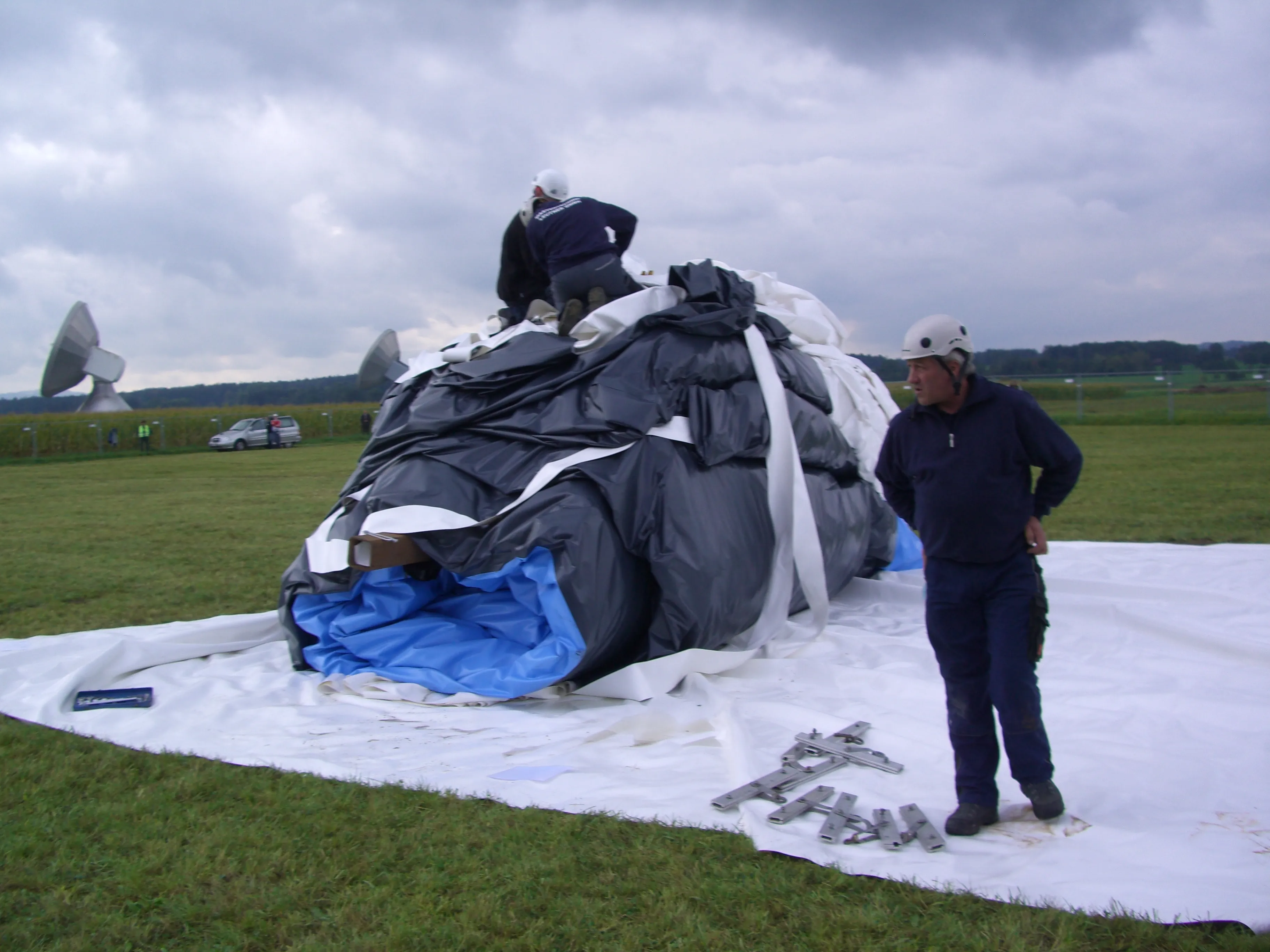 A membrana dobrada sendo preparada no local, com antenas parabólicas visíveis ao fundo.