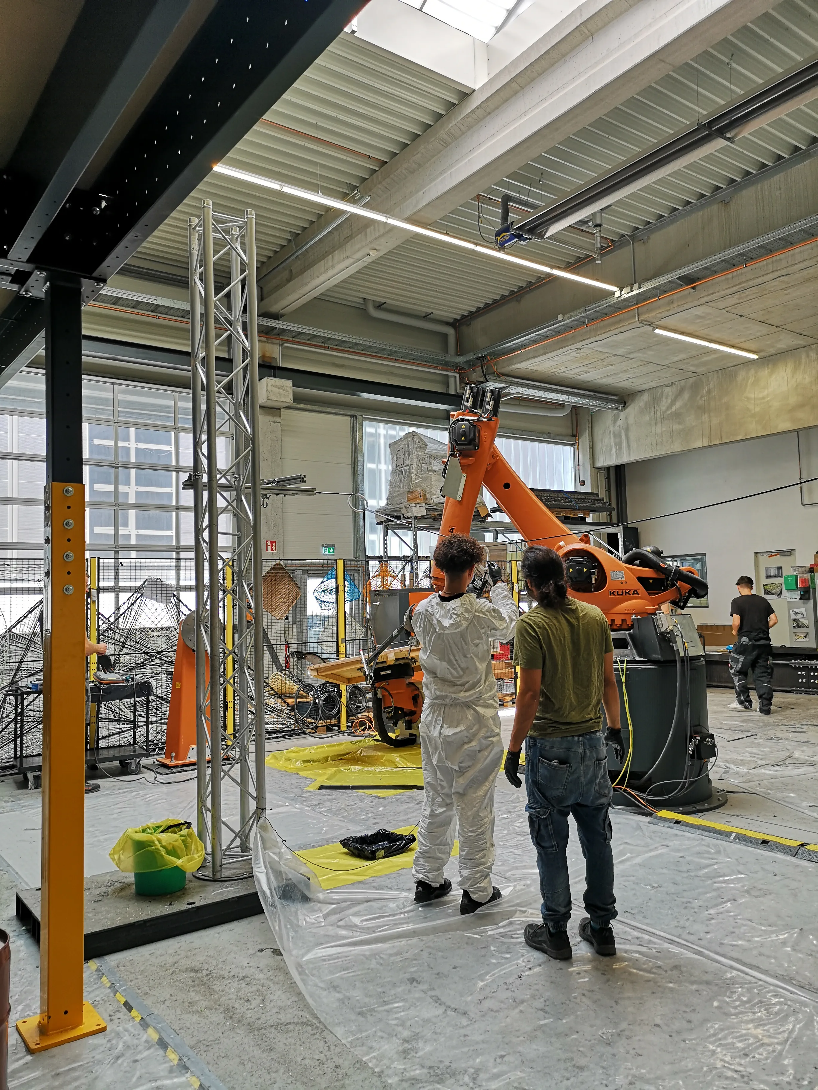 The robotic winding setup at the ICD Laboratory, showing the KUKA arm, winding frame, and protective floor covering.